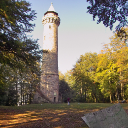 Oben auf dem Berg vor dem Humbergturm steht ein Junge mit einer Wanderkarte und blickt den Turm hinauf.