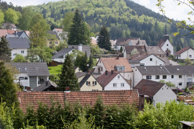 Mölschbach im Sommer. Die stark bewaldete, hügelige Landschaft erstreckt sich hinter den Häusern und der Kirche.