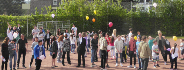 Beigeordneter Färber mit Schülerinnen und Schülern auf einem Sportplatz mit aufsteigenden Luftballons © Stadt Kaiserslautern