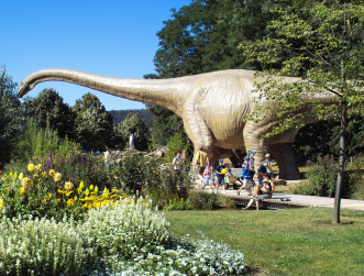 Ein großer Dinosaurier mit langem Hals steht in der blühenden Gartenschau.