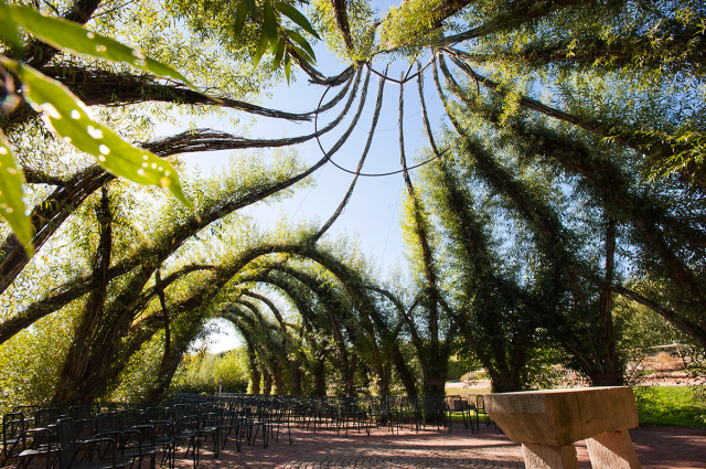 Auf dem Bild ist die Weidenkirche Gartenschau zu sehen. Im Vordergrund ist der Steinaltar.links und rechts gehen Säulen aus Weiden nach oben und treffen sich dann in der mitte oder ein paar überspannen den Innenraum und treffen auf der anderen Seite auf entgegenkommende Weideäste. Im Innenraum stehen viele Stühle. © view - die agentur