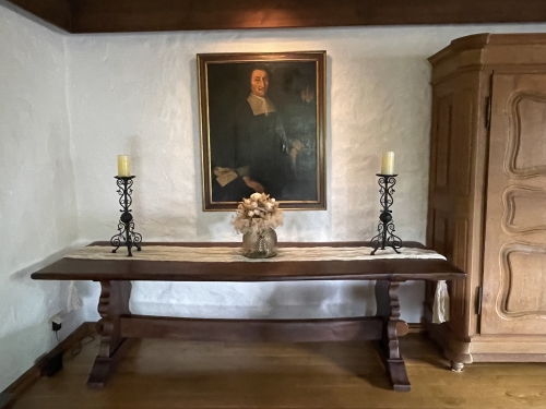 Blick ins Turmzimmer, hintere Ecke mit einem großen Holztisch. An der Wand dahinter ein Bild. 