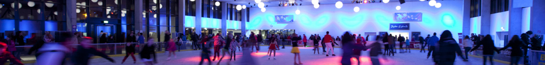 Die Eishalle ist in lilanes Licht getaucht und viele Jugendliche geben auf der Eisfläche Gas.