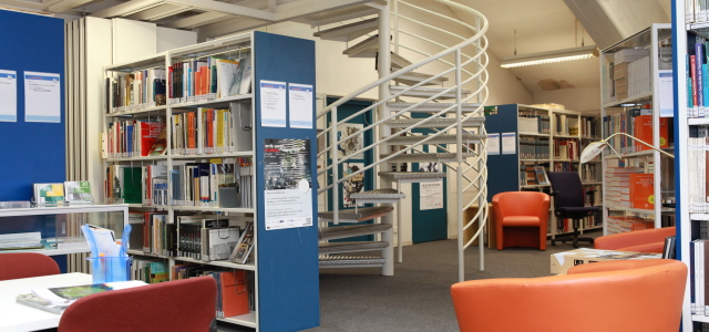 Eine einladende, kleine Bibliotheksecke mit vielen Sesseln als bequeme Sitzgelegenheiten. Über eine Wendeltrappe kann das nächste Stockwerk erreicht werden.