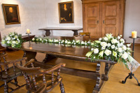 Der Tisch an dem das Paar getraut wird ist festlich geschmückt mit großen, weißen Blumensträußen.