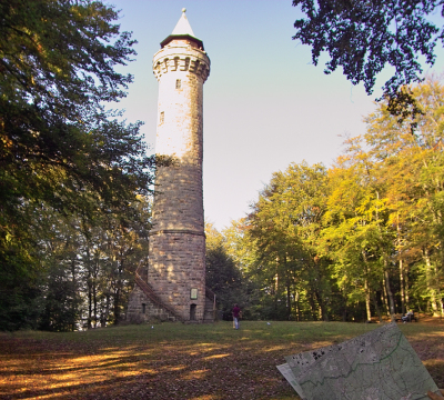 Oben auf dem Berg vor dem Humbergturm steht ein Junge mit einer Wanderkarte und blickt den Turm hinauf.