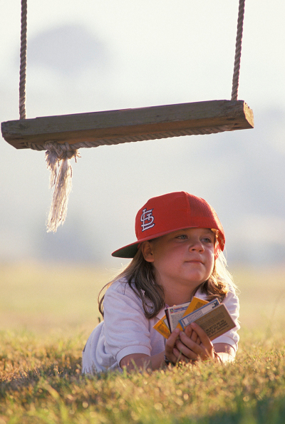 Ein Blick auf ein junges Mädchen mit roter Kappe, das mit Flyern auf dem Boden unter einer Holzschaukel liegt 