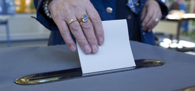 Eine ältere Dame gibt ihren Stimmzettel in die Wahlurne.