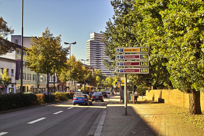 Man blickt die Rudolf-Breitscheid-Straße hinunter in Richtung Rathaus. Mehrere Autos und ein Bus fahren auf dieser Straße über eine grüne Ampel. Direkt vor dem Betrachter steht eine Bushaltestelle. © Stadt Kaiserslautern