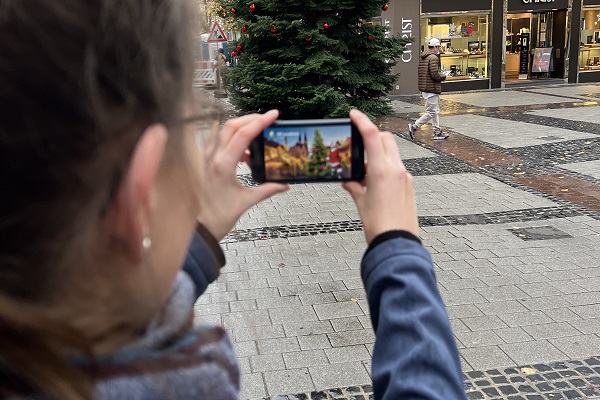 Eine Frau schaut sich ein Augmented-Reality-Bild der Tanne in der Fackelstraße auf ihrem Smartphone an.