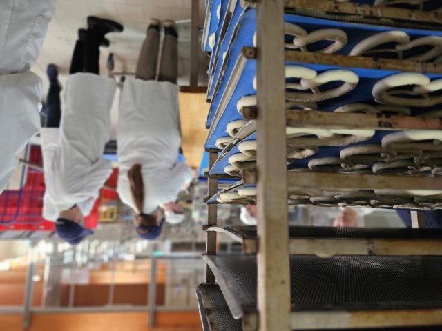 Ein Wagen mit Brezelteiglingen. Im Hintergrund unscharf die Besuchergruppe um OB Kimmel. © Stadt Kaiserslautern