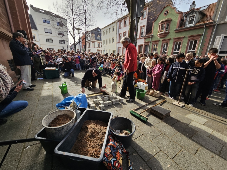 Beim Verlegen der Stolperschwelle. Im Hintergrund die Kinder der Schule. © Stadt Kaiserslautern