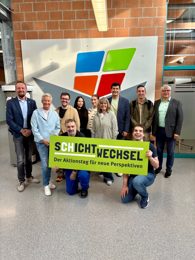 Die Gruppe um Beate Kimmel in den Westpfalzwerkstätten. Im Vordergrund halten zwei junge Männer ein Plakat Schichtwechsel hoch. © Ökumenisches Gemeinschaftswerk