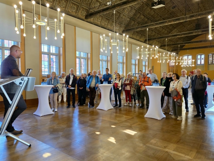 © Stadt Brandenburg Oberbürgermeister Daniel Keip bei der Begrüßung der Gäste aus Kaiserslautern im Rathaus. Er ist von hinten fotografiert, mit Blick in den Raum auf die Gäste, die an Stehtischen stehen. © Stadt Brandenburg
