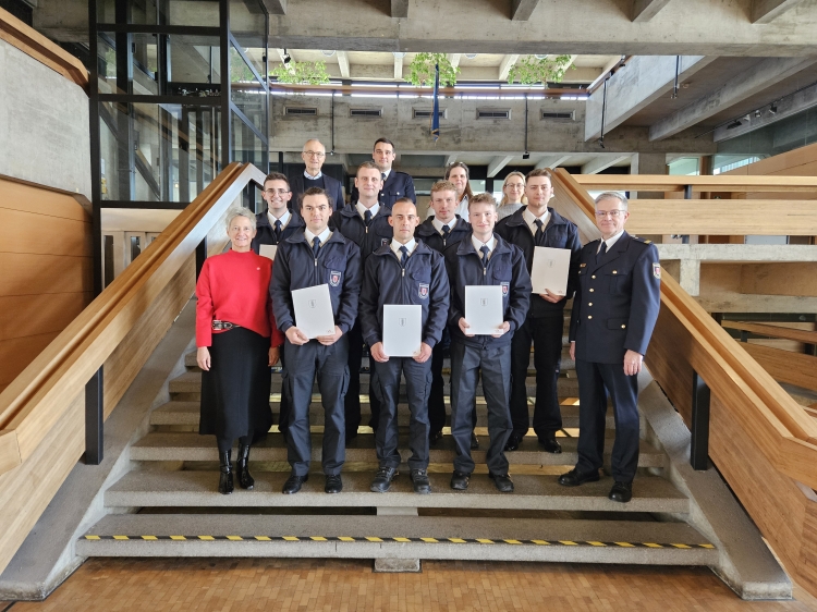 Die sieben neuen Feuerwehrmänner auf der Treppe im Rathausfoyer im Kreise ihrer Vorgesetzten, Ausbilder sowie Vertreterinnen und Vertretern von Personalreferat und Personalrat. Links vorne Oberbürgermeisterin Kimmel. © Stadt Kaiserslautern