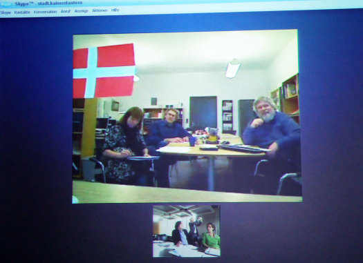 Videokonferenz mit Silkeborg. Auf dem Monitor sieht man ein Bild mit einer Frau und zwei Männern an einem Tisch. Sie lächeln freundlich in die Kämera. © Stadt Kaiserslautern