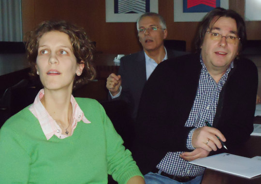 Frau im grünen Pullover und ein Mann im karierten Hemd mit Sakko hören interessiert einem Vortrag zu © Stadt Kaiserslautern