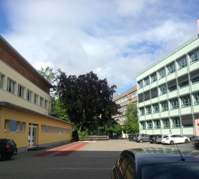 Innenhof des St.-Franziskus-Gymnasiums und Realschule mit parkenden Fahrzeugen mit Blick auf die Sprunggrube
