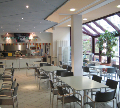 Cafeteria HSG - Stühle und Tische mit großer Fensterfront. Im Hintergrund Bedientheke
