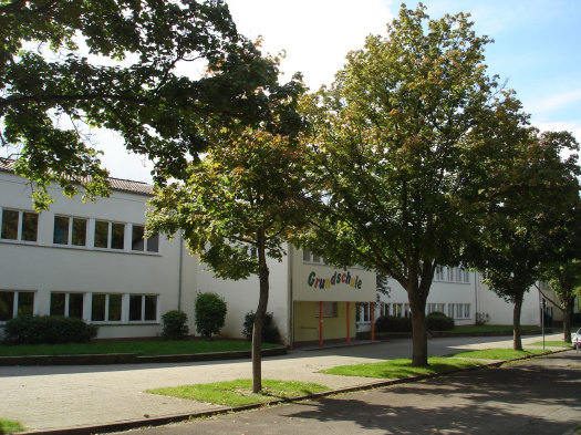 Schulgebäude mit Laubbäumen davor. Grundschule steht in bunten Buchstaben an der Hauswand. © Grundschule Geschwister-Scholl