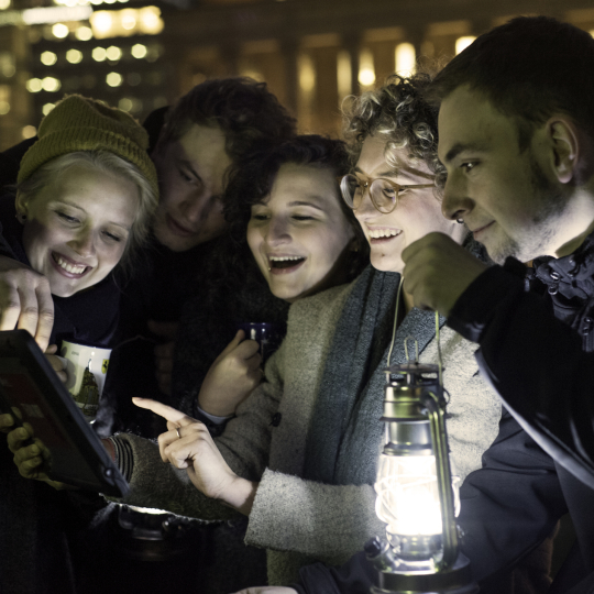 nächtliche Straßenszene: Gruppe junger Menschen in mit Tablet und Großer Handlampe