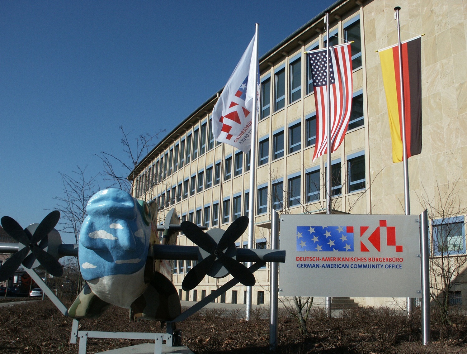 Das rathaus Nord mit dem internationalen Fliegerfisch, dem Deutsch-Amerikanischen Bürgerbüro Schild und gehissten Flaggen deutscher und amerikanischer Nationalität.