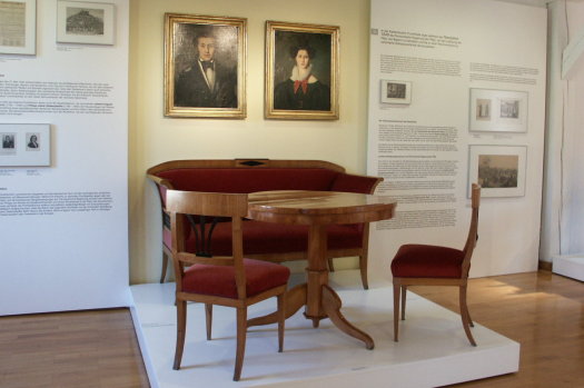 Eine Einrichtung aus der Biedermeierzeit. Die Stühle und die Bank ist aus Holz und mit rotem Bezug überzogen.  © Theodor-Zink-Museum