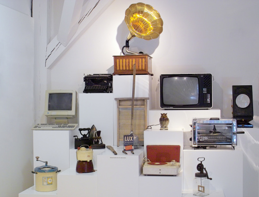 Zu sehen ist ein Grammophon, ein alter Röhrenmonitor, eine Schreibmaschine, ein Röhrenfernseher mit Bedienelementen an der Seite, eine alte Reibe, ein Bügeleisen, ein Grill und ein Plattenspieler. © Theodor-Zink-Museum