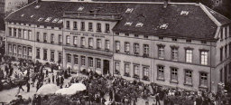 Eine Fotografie, die das alte Gebäude des Museums zeigt. Der Stiftsplatz vor dem Gebäude ist stark belebt, u.a. wegen den aufgebauten Marktständen.