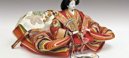 Eine japanische Puppe. Mit weißer Schminke, ausladender rötlicher Kleidung und einem Fächer.