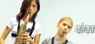 Zwei junge Musikerinnen mit ihren Saxophonen. Passend dazu ist eine Notenzeile mit Violinschlüssel im Hintergrund zu sehen.