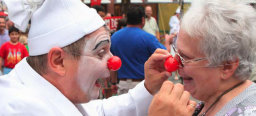 Ein Clown mit roter Nase setzt einer älteren Dame ebenfalls eine rote Nase auf. Diese nimmt es mit viel Humor.