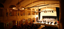 Nur die Bühne des großen Saals mit dem Orchester wird beleuchtet, der Rest ist in Dämmerlicht getaucht. Das Publikum lauscht andächtig und verfolgt die Bewegungen des Dirigenten.