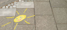 eine mit gelber Straßenkreide auf Gehwegplatten gemalte strahlende Sonne 