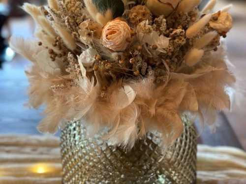 Silberne Vase mit geschackvollen Kunstblumen eingerahmt mit weichen Daunenfedern