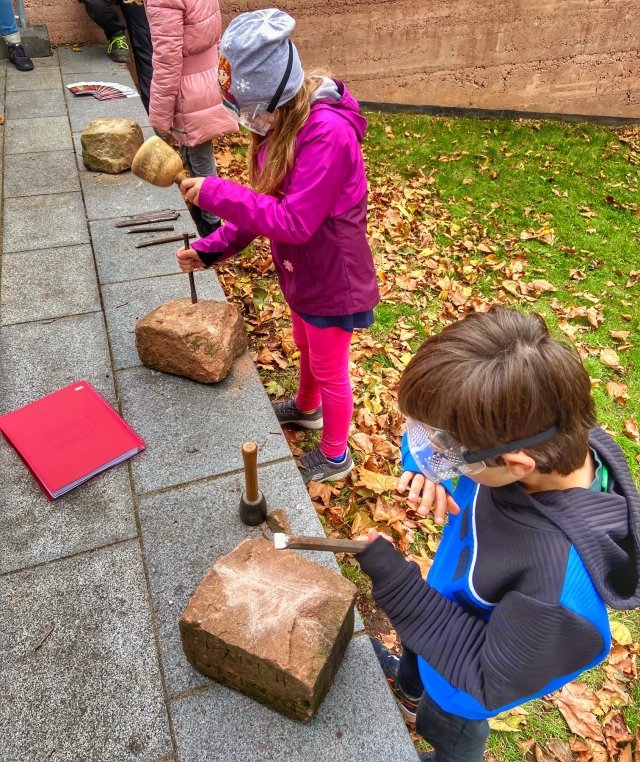 Kinder mit Schutzbrille, die an der Kaiserpfalz Steinblöcke mit Hammer und Meißel bearbeiten.  © Petra Rödler