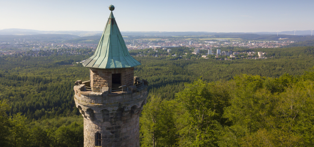 Im Vordergrund sieht man die Spitze des Humbergturmes und im Hintergrund die Stadt und den Pfälzerwald.