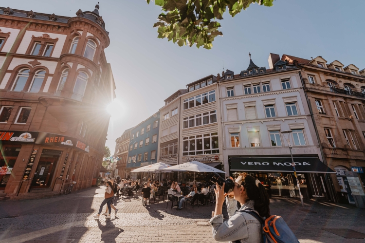 Thomas Linkel, Lizenz CC-BY Man sieht den Platz vor der Stiftskirche im Sommer. Im Vordergrund eine Frau, die ein Gebäude fotografiert. Im Hintergrund Außengastronomie. Thomas Linkel, Lizenz CC-BY