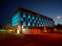 The block-like designer hotel shines at night in bluish colors.