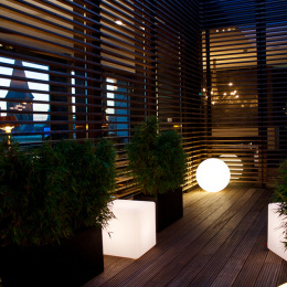 An open area on the roof where geometric lamps and green plants standing on a wooden plank and box-shaped vases.
