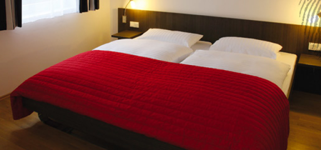 Ein großes Doppelbett mit roter Tagesdecke.