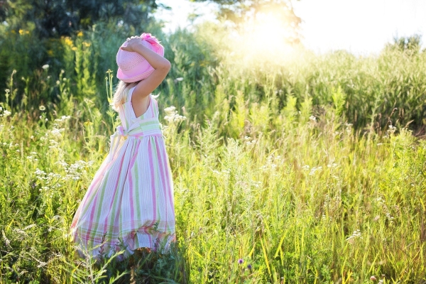 Kind in Kleid mit Hut auf einer sommerlichen Wiese.