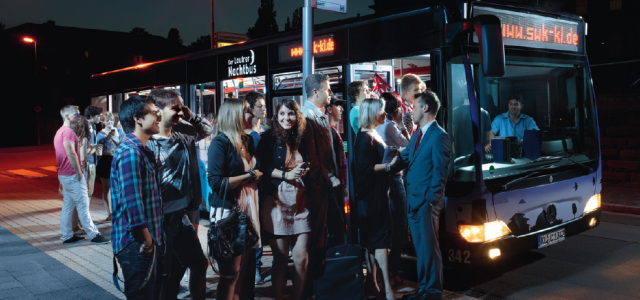 Gruppe von Nachtschwärmern an einer Haltestelle beim Einsteigen in den Nachtbus