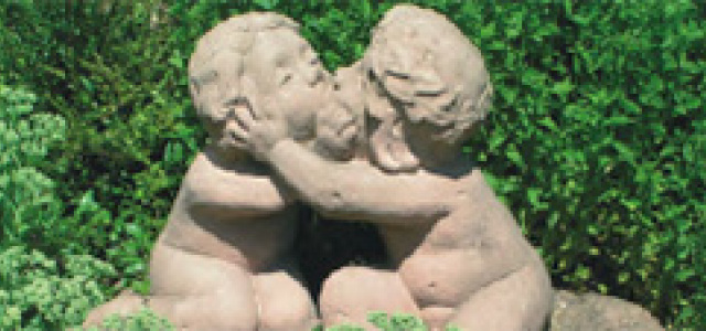 Sandsteinplastik zeigt zwei unbekleidete kindliche Gestalten, sich innig umarmend auf einem Kissen
